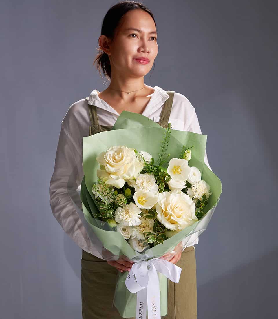 Ivory roses and white chrysanthemums bouquet with green foliage, wrapped in soft green paper and white ribbon