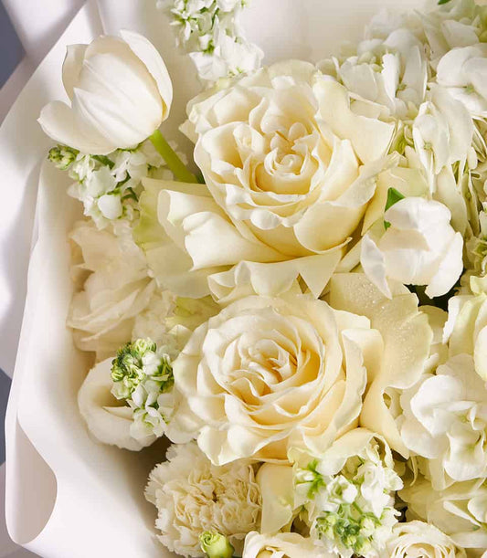 Ivory roses and white lilies fresh flower bouquet with cream tulips and filler flowers, wrapped in soft white paper
