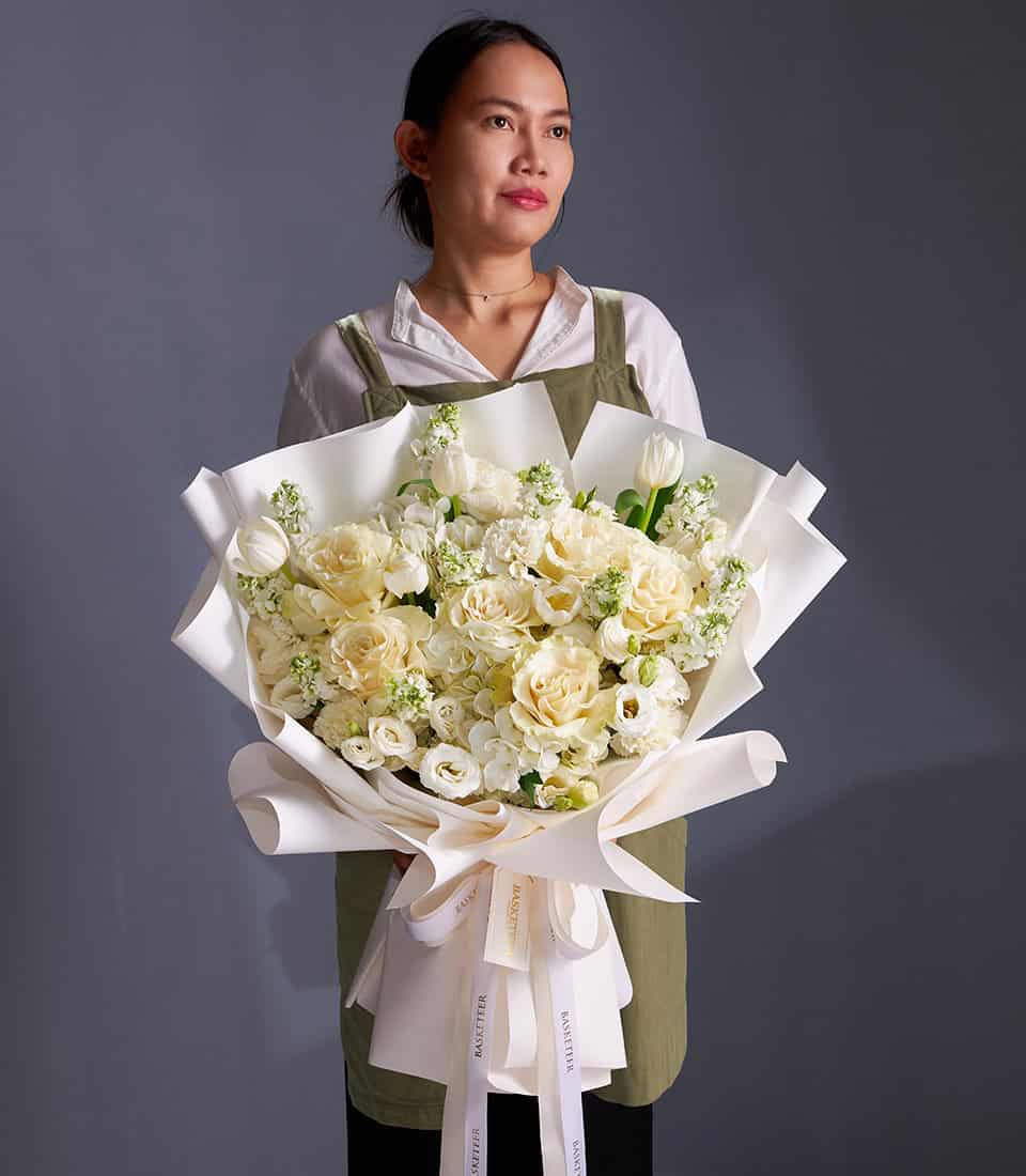 Ivory roses and white lilies bouquet with cream filler flowers, elegantly wrapped in white paper with ribbon