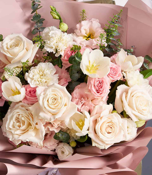 Ivory and blush roses with white tulips in soft pink wrapping, premium fresh flower bouquet