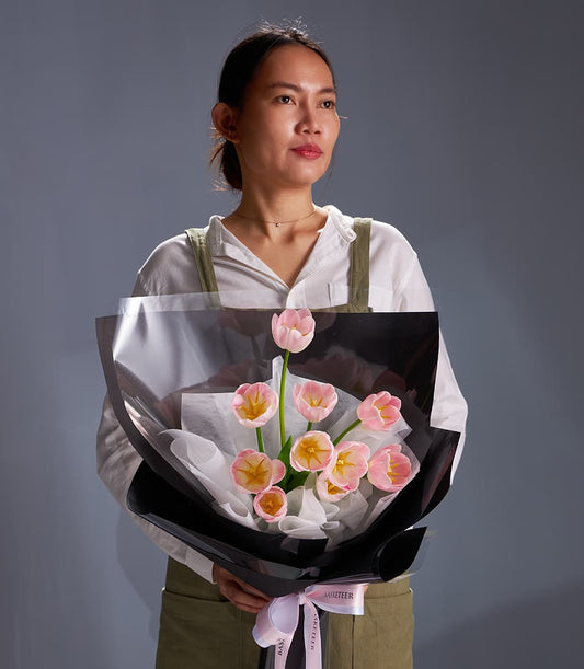 Pastel pink tulip bouquet with yellow centers, wrapped in black cellophane and white tissue paper