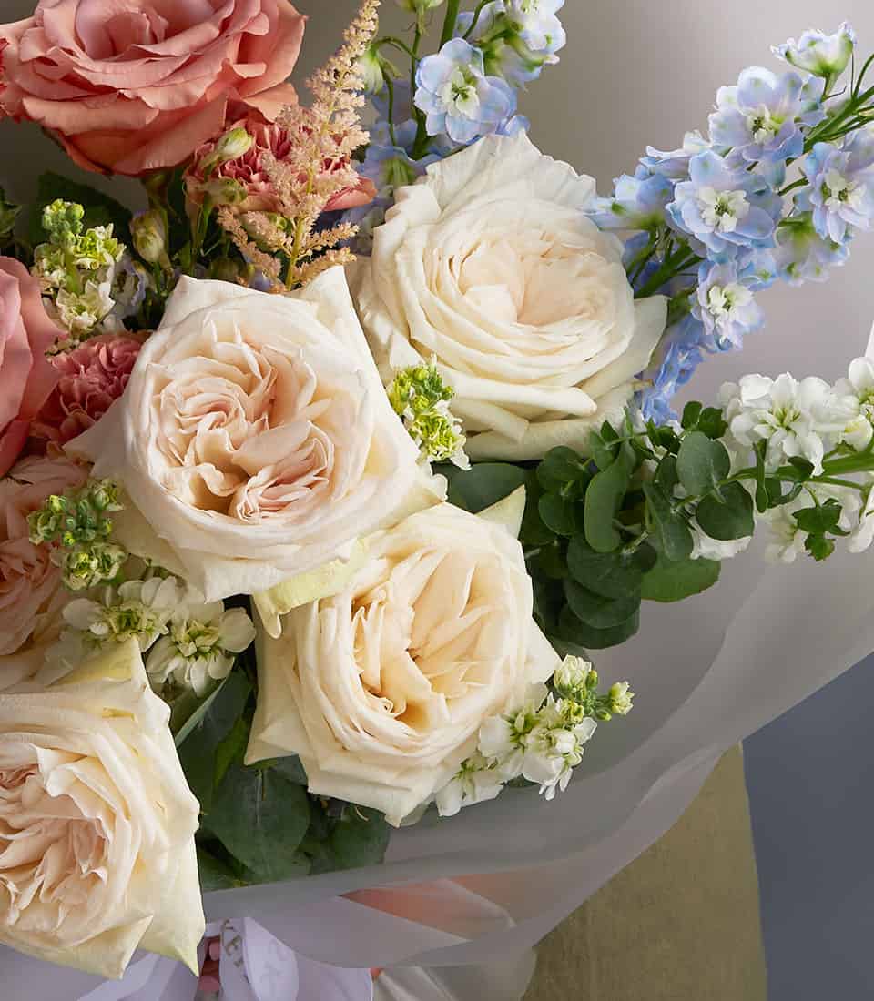 Ivory rose and blue delphinium bouquet with astilbe and eucalyptus, wrapped in white paper
