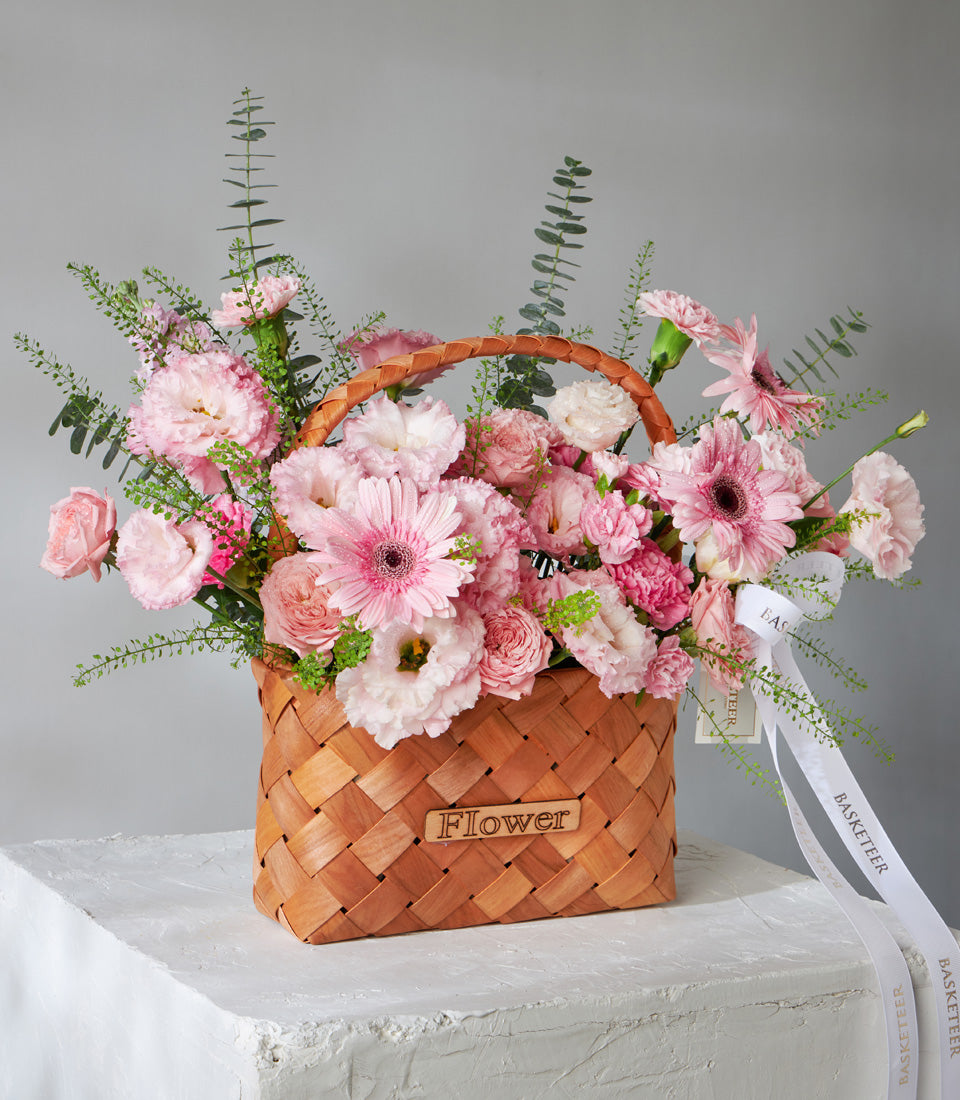Vibrant pink and white gerbera daisies, roses, and carnations in woven wooden basket with eucalyptus, birthday gift