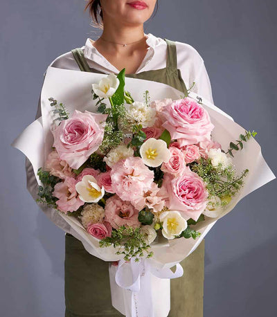 Blush pink roses and white tulips fresh flower bouquet wrapped in white paper with ribbon