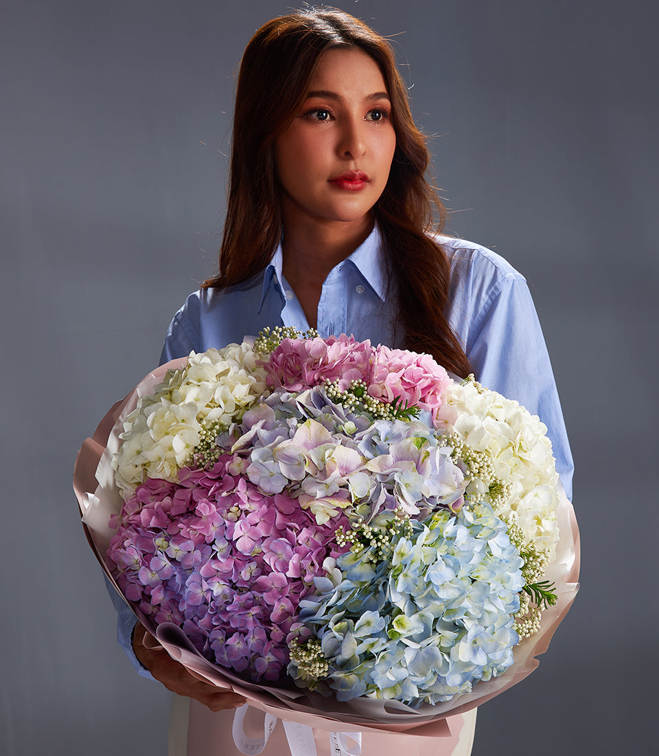 Premium vibrant hydrangea bouquet in white, pink, blue, and purple with white filler flowers, wrapped in pink paper