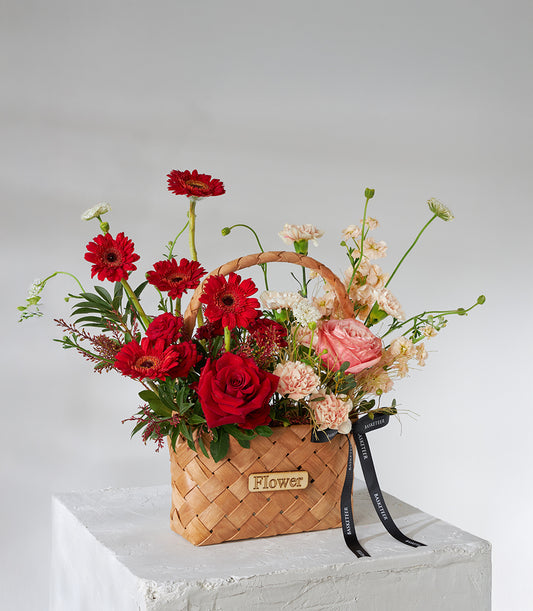 Crimson roses and gerbera celebration basket with pink carnations in woven wooden carrier