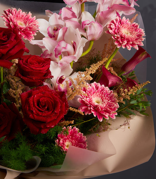 Red roses, pink gerberas, and orchids with burgundy calla lilies in artisan wrapped bouquet