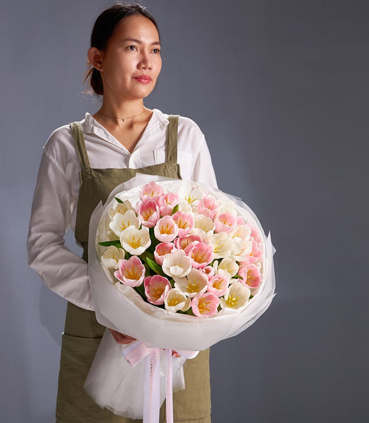 Fresh pastel pink and white tulip bouquet wrapped in white paper with pink ribbon