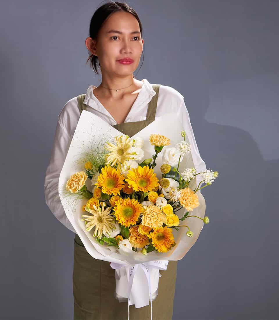 Bright yellow gerbera daisies and white chrysanthemums bouquet with green foliage, wrapped in white paper and ribbon