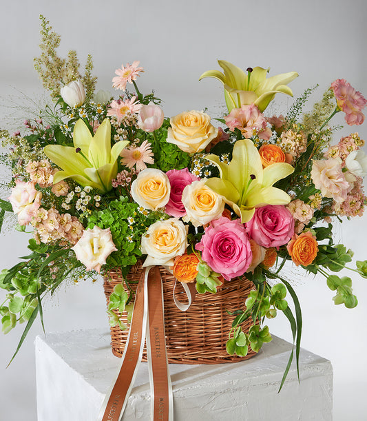 Fresh yellow lilies and pink roses in woven basket with mixed blossoms and greenery