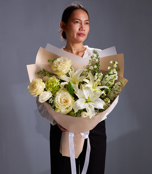 Elegant white lily and cream rose bouquet with hydrangea, wrapped in beige paper and white ribbon