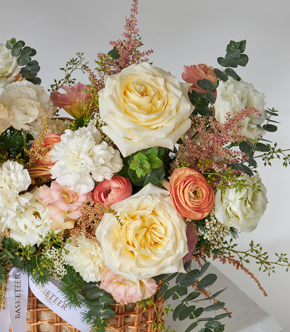Peach and cream roses with white carnations in woven gift basket, premium fresh flower arrangement