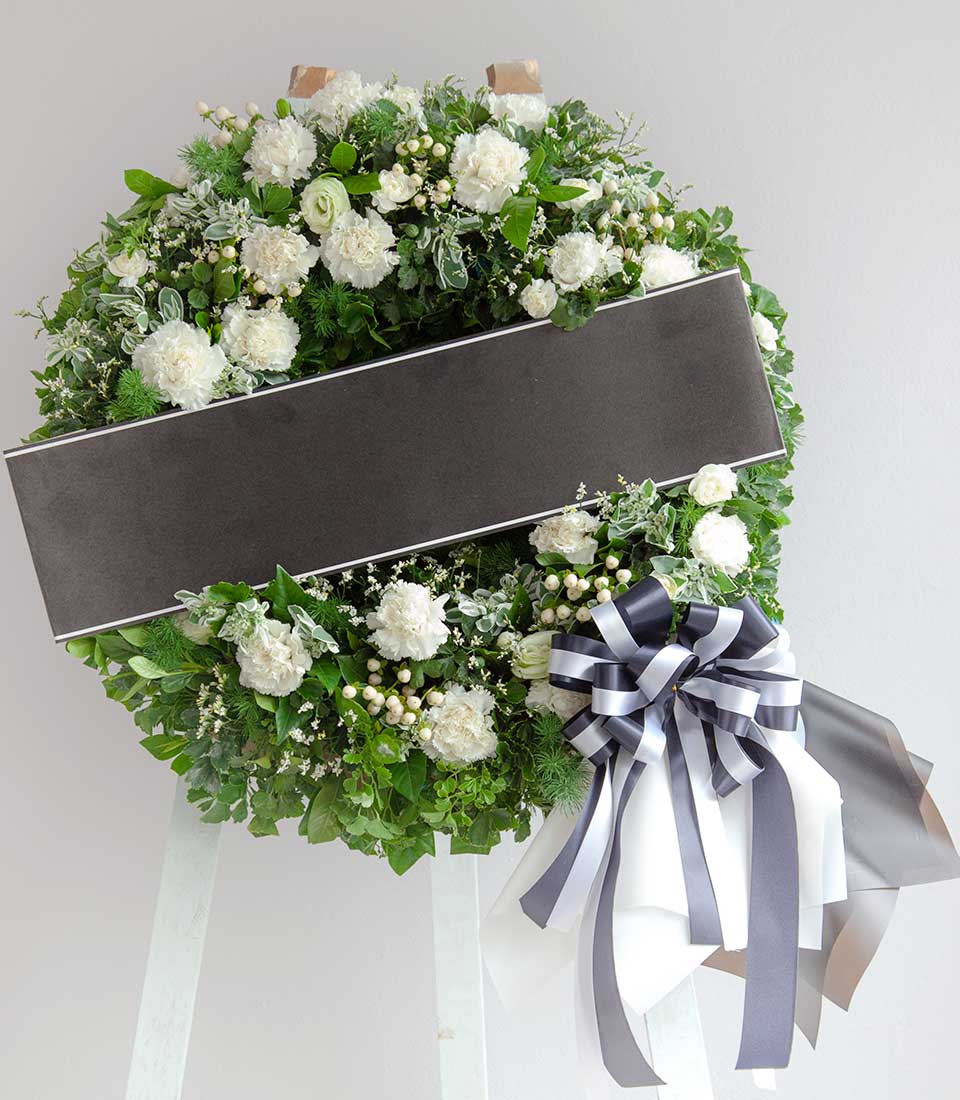 White and green funeral wreath with carnations, grey ribbon banner, and elegant tribute bow