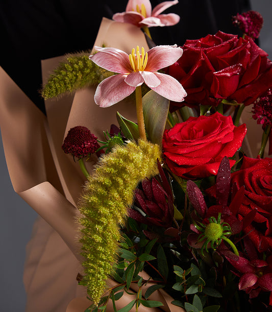 Red roses and pink lilies with burgundy accents in fresh wrapped bouquet for gifting