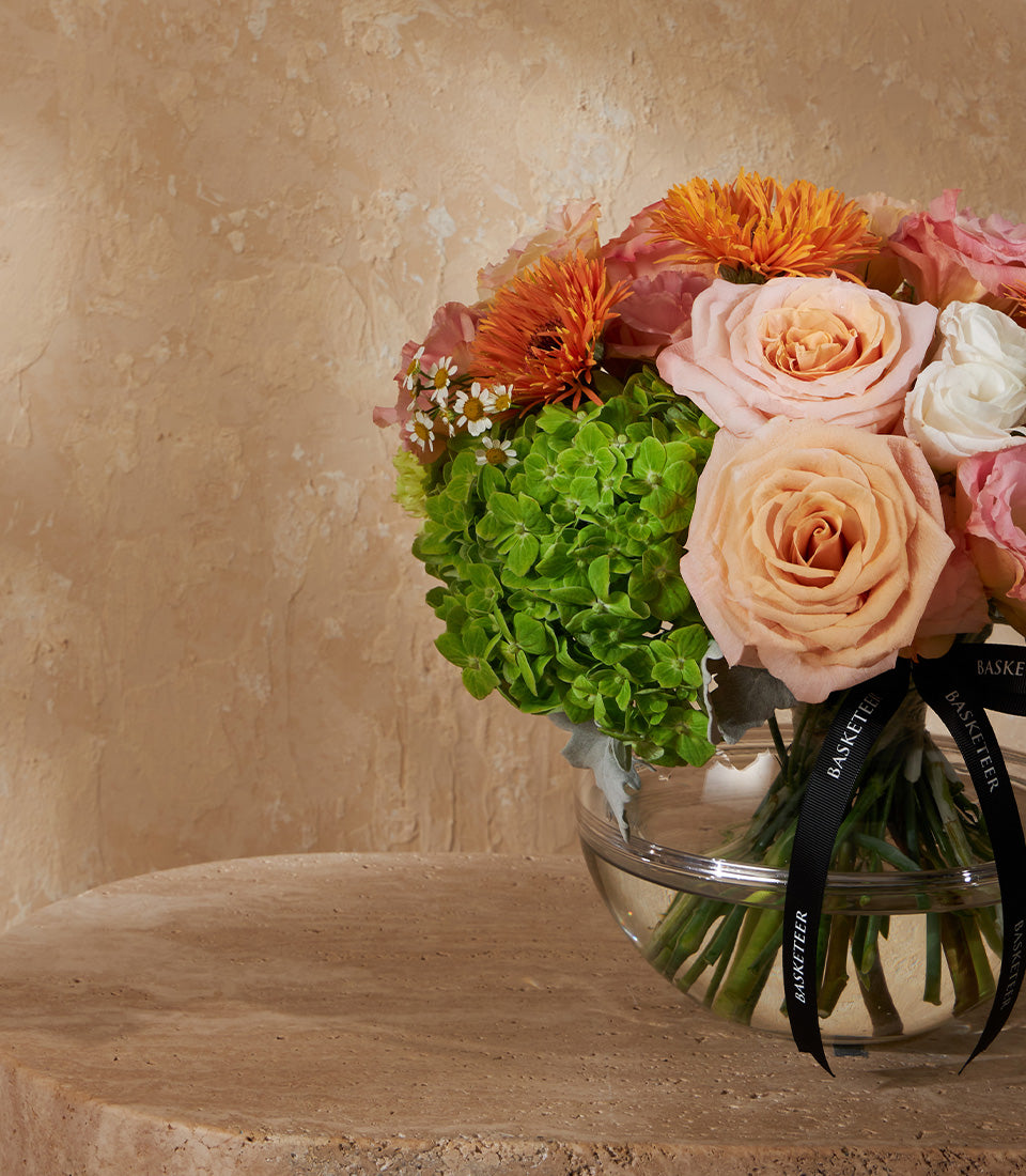 Radiant Harmony peach and pink rose vase arrangement with orange fringed flowers and white daisies in clear glass bowl