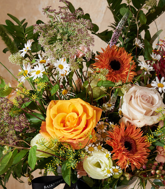 Radiant Charm vase arrangement with orange roses, peach blooms, and white daisies in warm earth tones