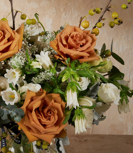 Burnt orange and cream roses with baby's breath in clear glass vase, tied with black ribbon