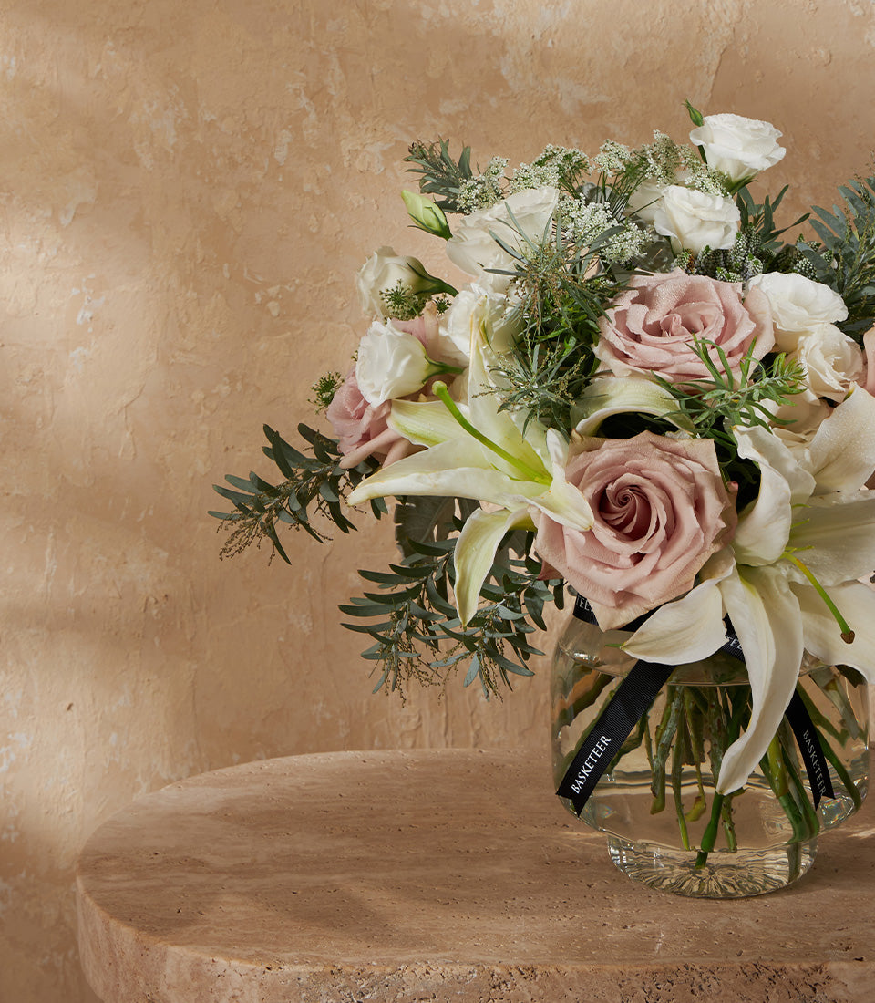 White and dusty pink roses with lilies in clear glass vase, tied with black ribbon