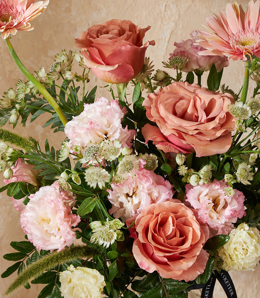 Dusty rose and peach Moab roses with pink Lisianthus and white filler flowers in a fresh vase arrangement