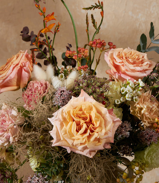 Peach and pink rose vase arrangement with carnations, berries, and textured botanicals