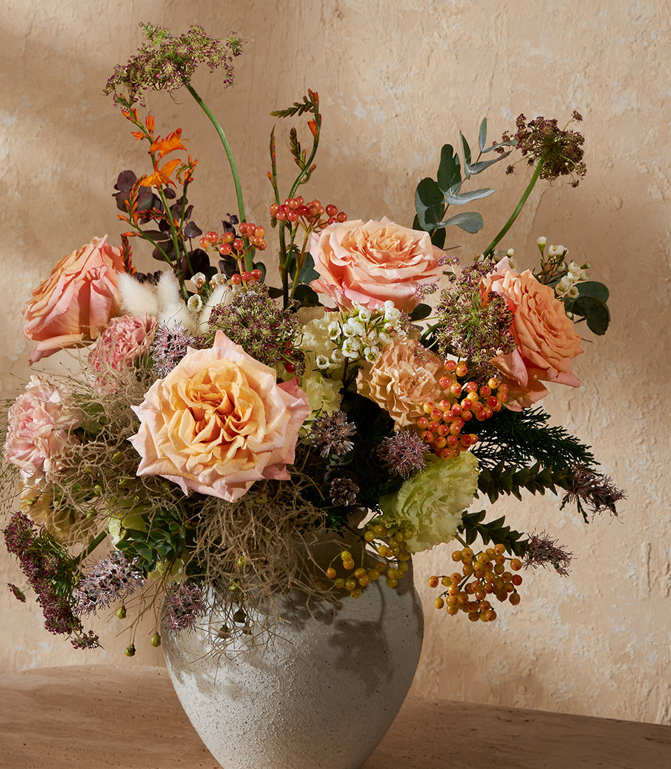 Peach and pink roses with berries in textured grey ceramic vase, artisan flower arrangement