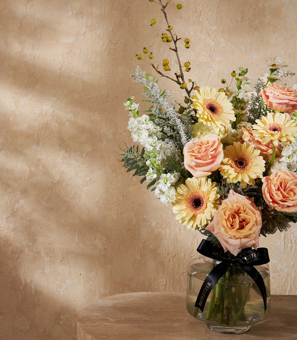 Golden Harmony premium flower arrangement with yellow gerberas, peach roses, and white stock in clear glass vase