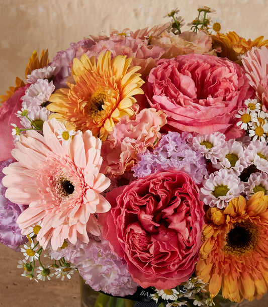 Vibrant mixed rose and gerbera arrangement in pink, coral, orange and yellow in clear glass vase