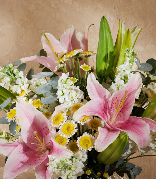 Vibrant pink lily floral arrangement with white stock flowers and yellow daisies in lush green foliage