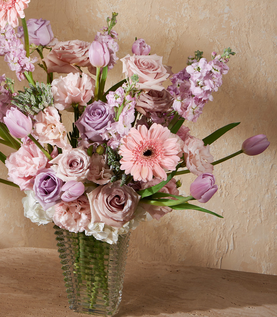 Lavender and peach mixed fresh flowers in textured glass vase with roses and greenery