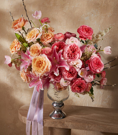 Radiant peach and pink rose arrangement with lilies and ranunculus in clear glass vase with silver base