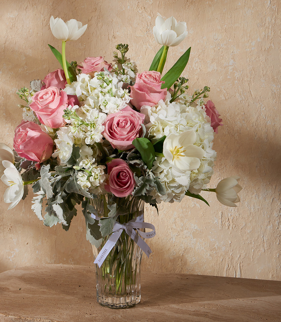 Pink roses and white hydrangeas in a clear glass vase with dusty miller foliage, tied with signature Basketeer ribbon