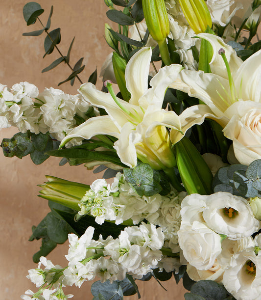 Elegant white lily vase arrangement with roses, stock flowers, and eucalyptus greenery