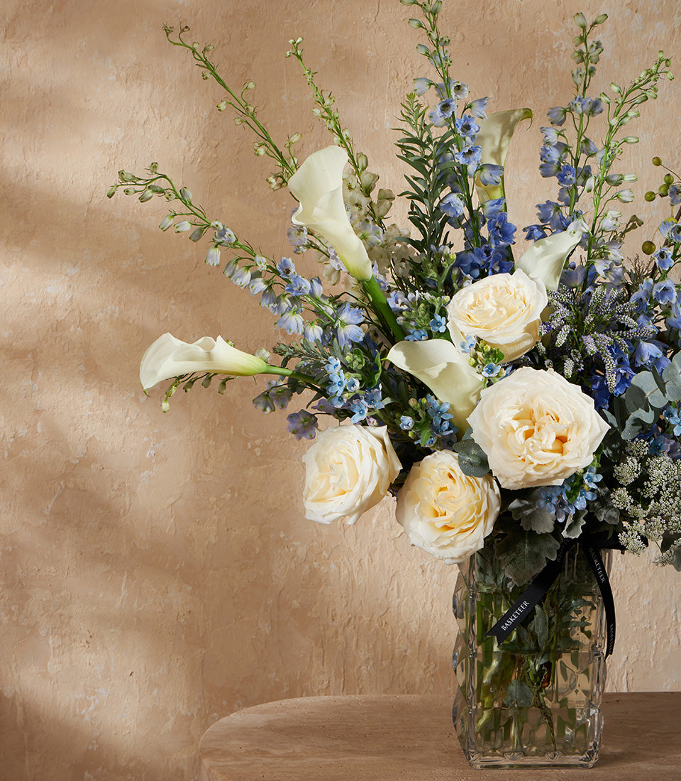 White calla lilies and garden roses with blue delphiniums in textured glass vase