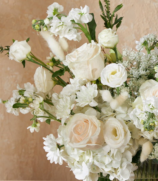 White roses and cream flowers in clear glass vase with baby's breath and bunny tail grass