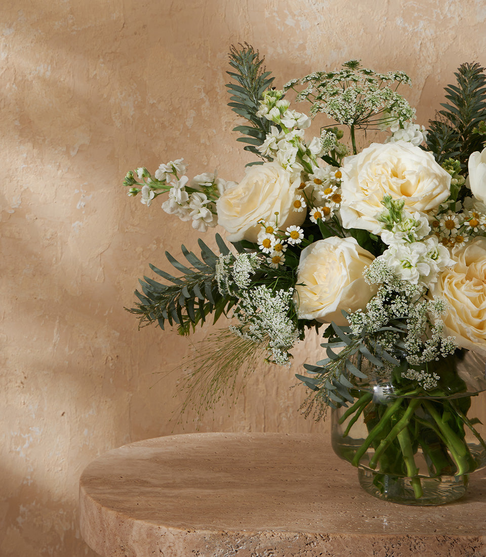 Premium white and cream rose arrangement with stock and chamomile in clear glass vase