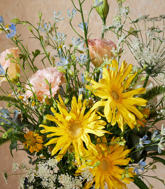 Vibrant yellow daisy bouquet with blue bells, pink roses, and white flowers in a luxury vase arrangement
