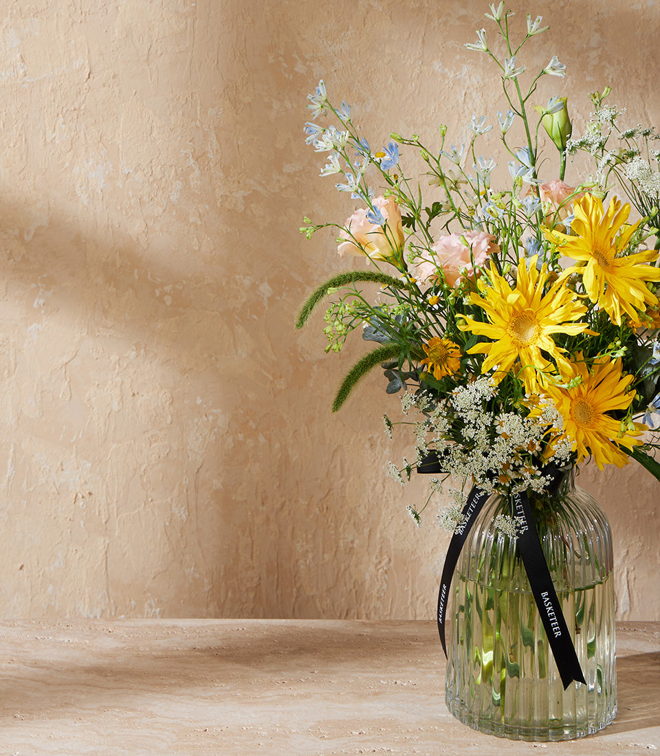Vibrant yellow roses with white filler flowers and soft pink blooms in clear ribbed glass vase