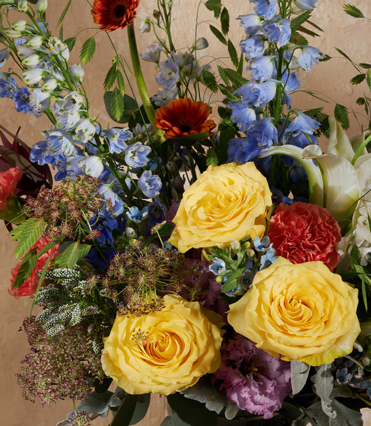 Vibrant yellow roses with blue delphiniums and orange gerbera in elegant vase arrangement
