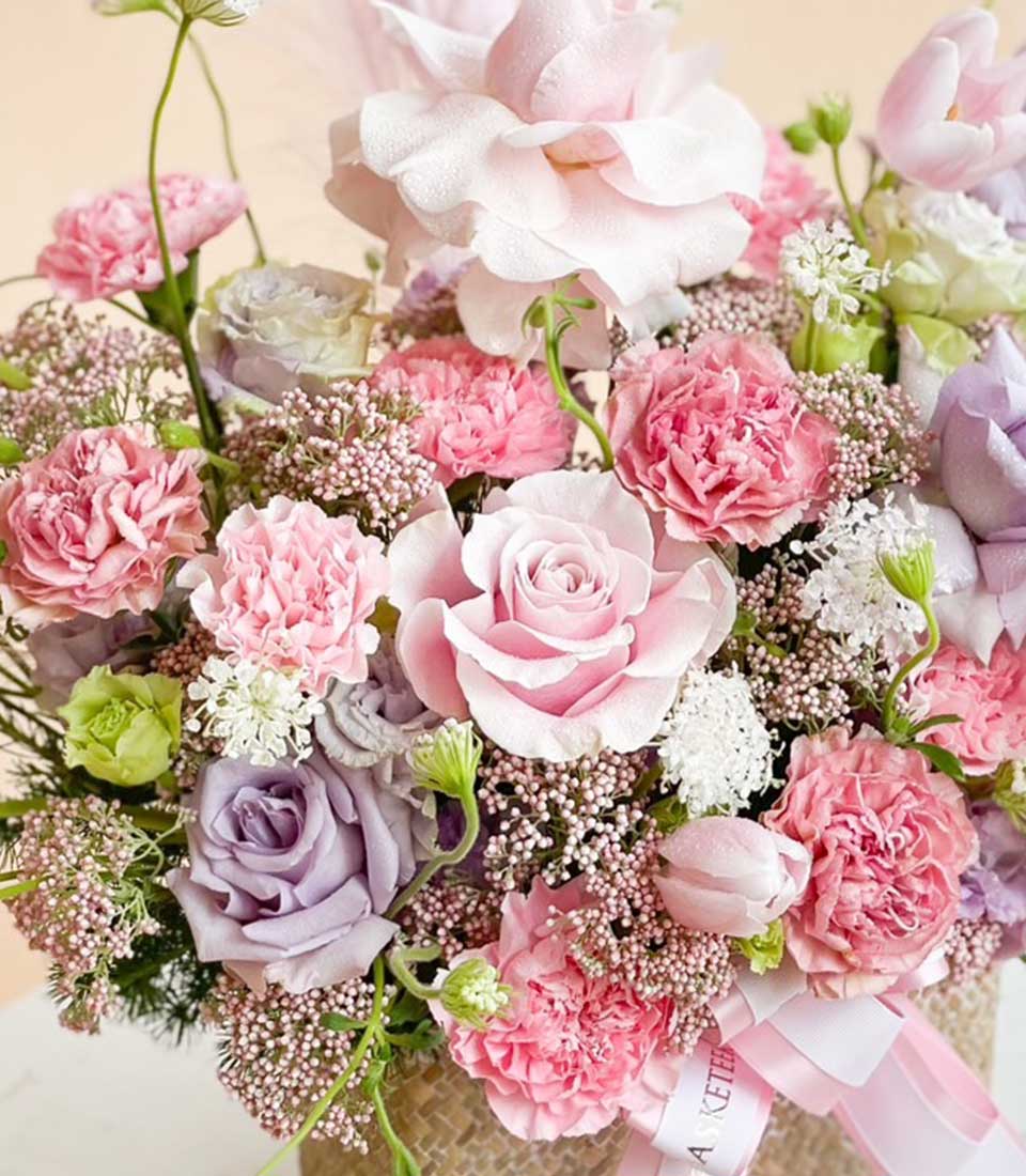 Pink and purple roses with carnations in a woven basket with pink ribbon, get well flowers arrangement