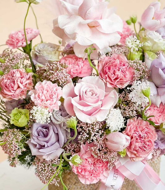 Pink and purple roses with carnations in a woven basket with pink ribbon, get well flowers arrangement