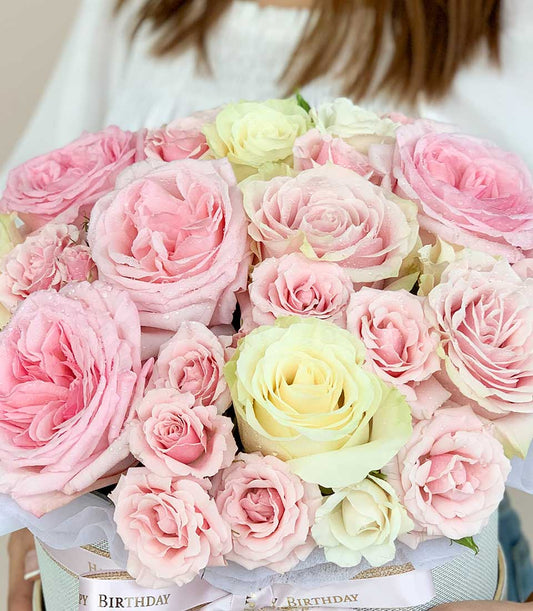 Pink and yellow fresh roses with water droplets in luxury hatbox, adorned with Happy Birthday ribbon