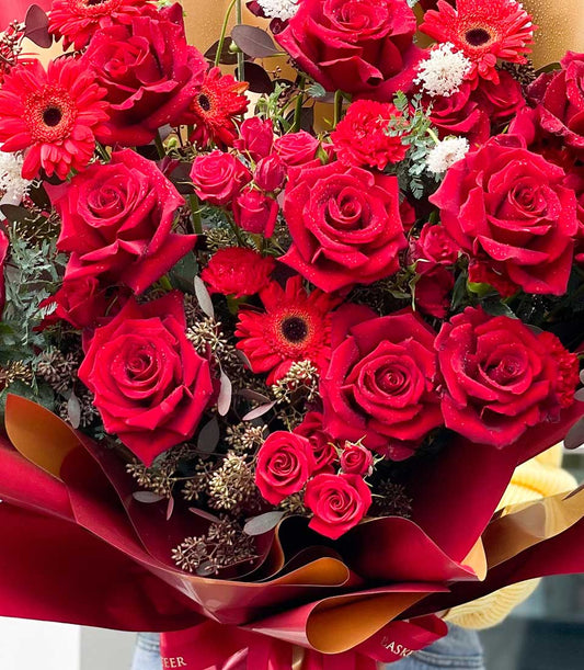 Vibrant red rose and gerbera bouquet with crimson carnations, wrapped in luxe dark red paper with gold lining