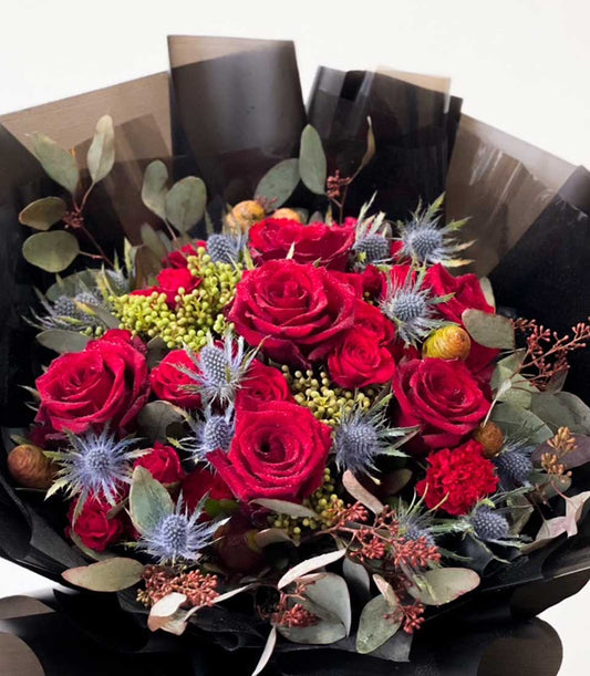 Deep red roses with blue thistles and eucalyptus in black-wrapped luxury bouquet