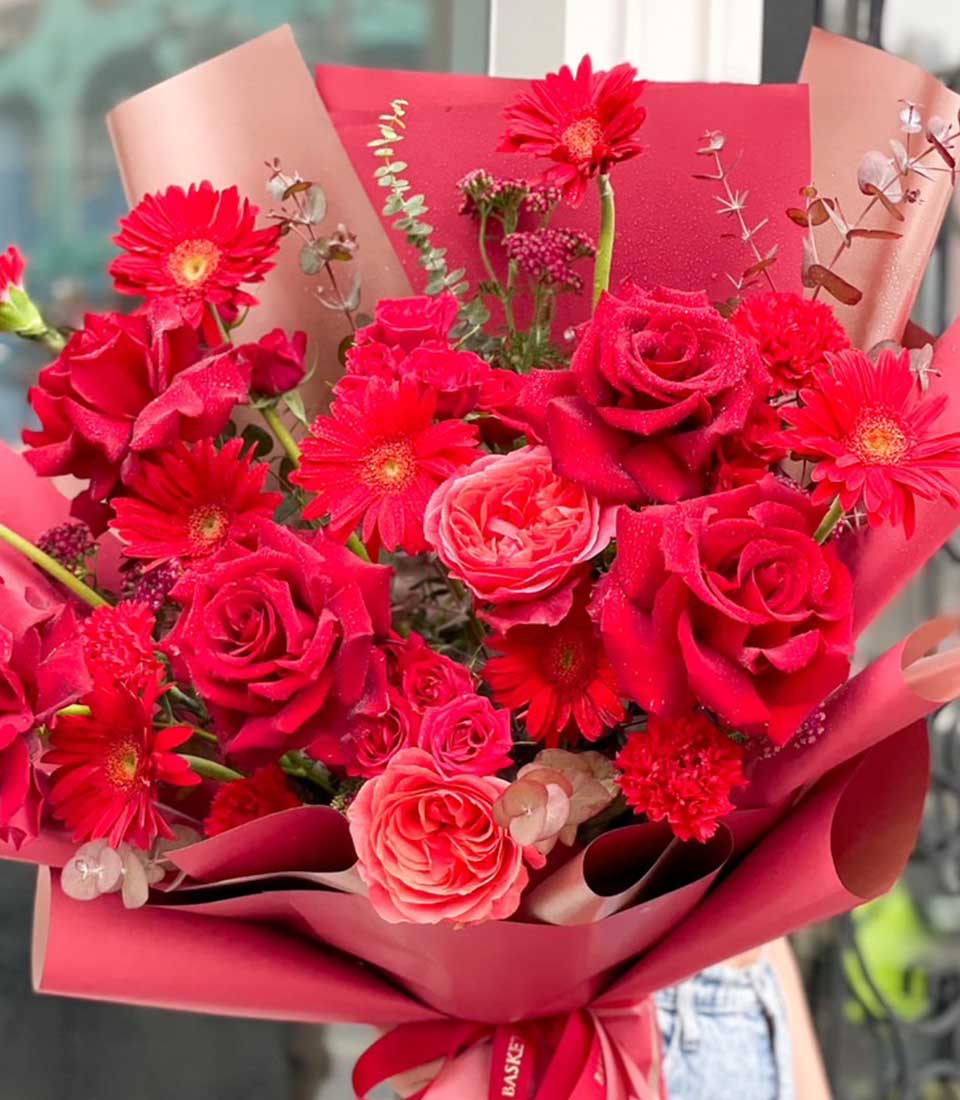 Vibrant red and pink rose bouquet with gerbera daisies, wrapped in red paper with ribbon bow