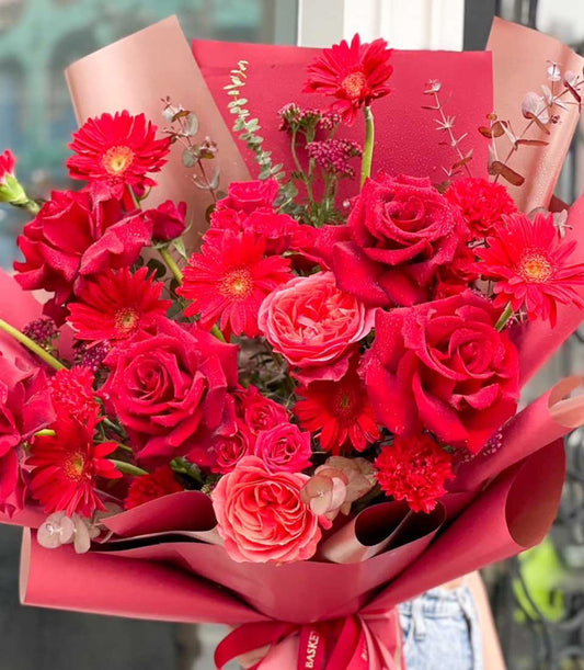 Vibrant red and pink rose bouquet with gerbera daisies, wrapped in red paper with ribbon bow