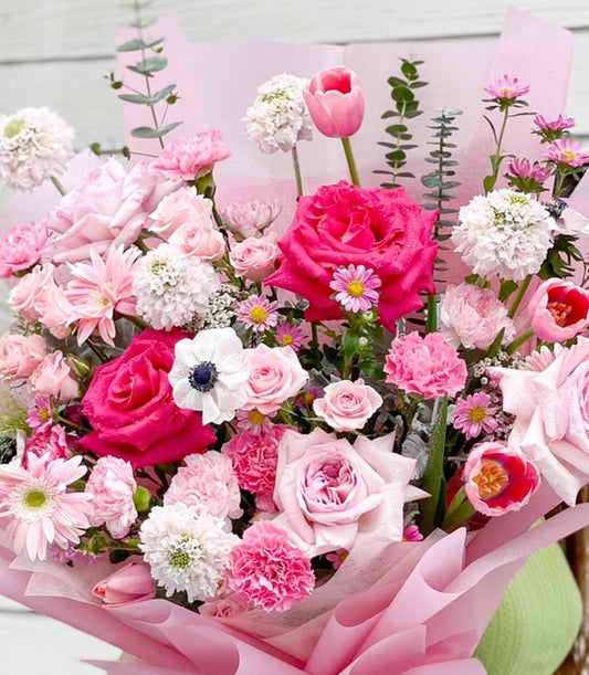 Vibrant pink and white rose bouquet with anemones, carnations, and tulips in soft paper wrapping