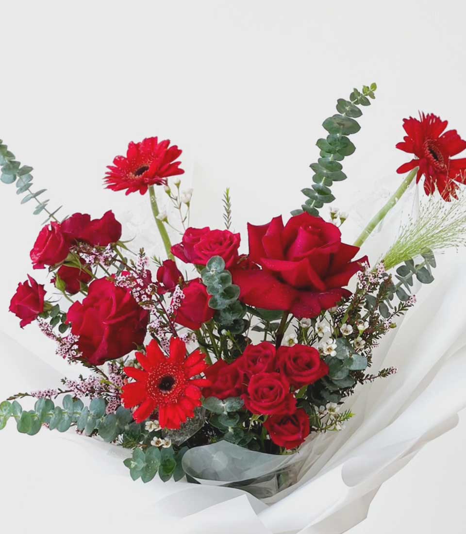 Red roses and gerbera daisies bouquet with eucalyptus, wrapped in white paper for graduation