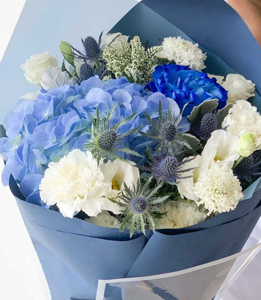 Vibrant blue hydrangea and white rose graduation bouquet with blue thistle accents, wrapped in coordinating blue paper