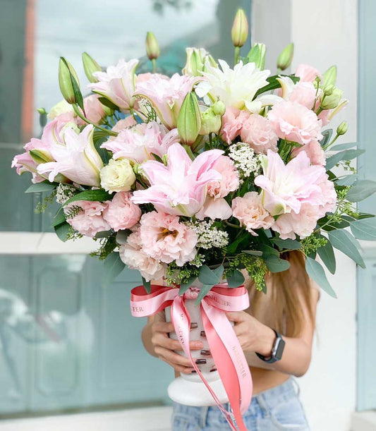 Elegant pink lily arrangement in white fluted vase with eustoma and eucalyptus, tied with pink ribbon bow