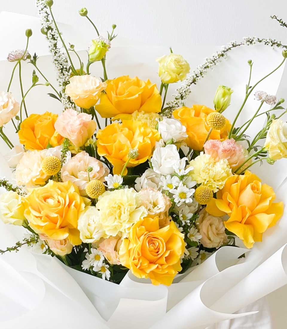 Bright yellow roses and ranunculus graduation bouquet with white paper wrap